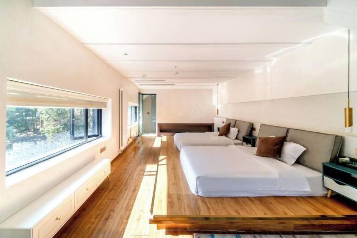 A modern bedroom with a large window, a bed with a wooden headboard, and a bedside table.