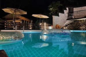 A swimming pool with clear water, surrounded by umbrellas and a stone wall. - Heshi Mogan Hotel (Deqing)