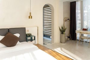 Quarto de hotel moderno com cama, mesa de cabeceira, luminária, escrivaninha, cadeira e um vaso de planta.