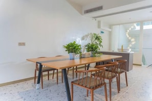 A modern dining area with a wooden table and chairs, potted plants, and a kitchen counter in the background. - Heshi Mogan Hotel (Deqing)