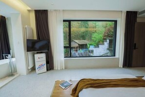 A hotel room with a large window, a bed, a television, and a refrigerator. - Heshi Mogan Hotel (Deqing)