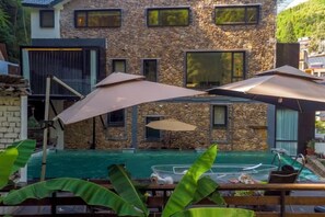A stone building with a pool, outdoor umbrellas, and a wooden deck. - Heshi Mogan Hotel (Deqing)