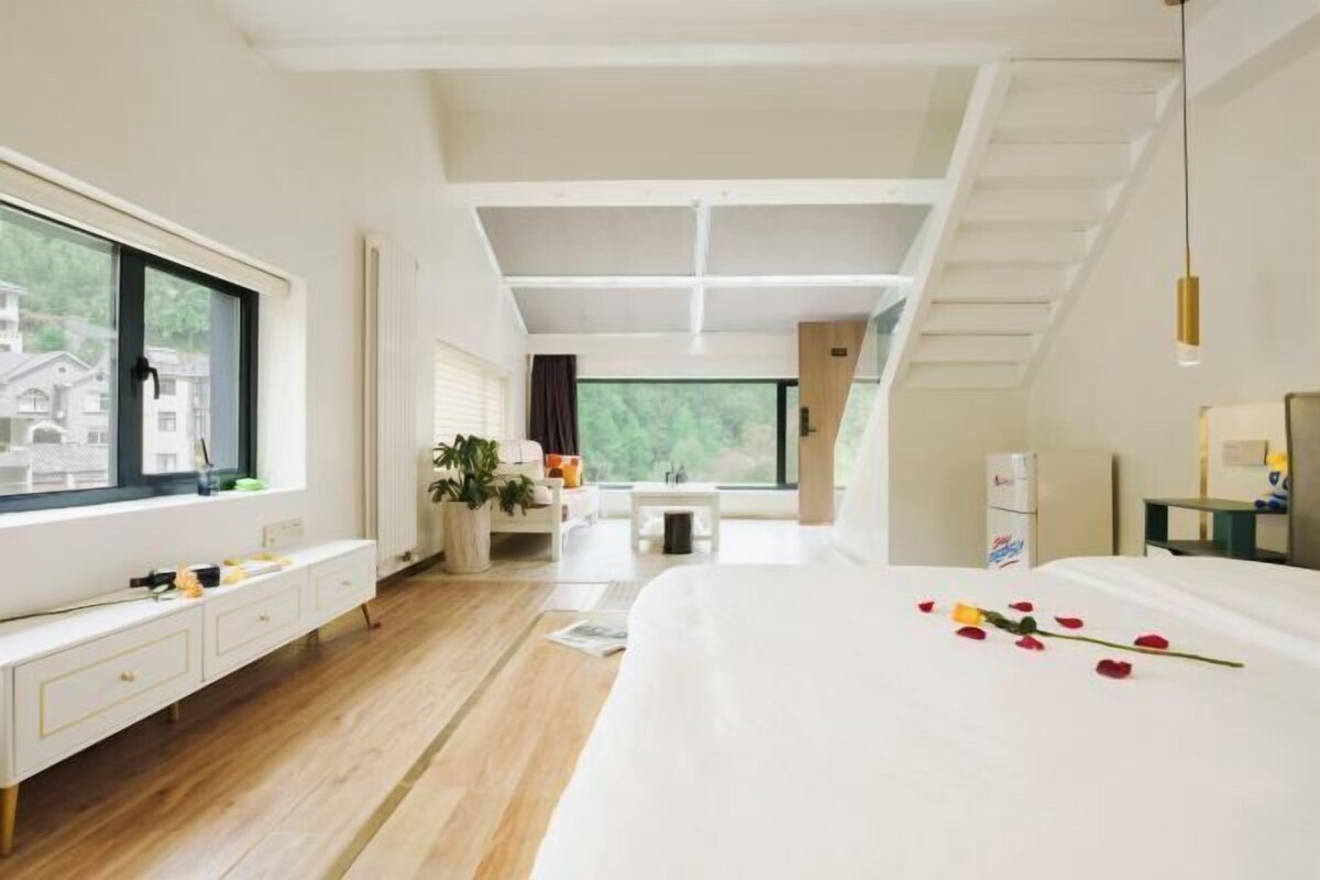 A modern hotel room with a large bed, a window with a view, a desk, and a staircase.
