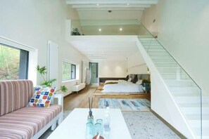 A modern interior with a sofa, a white coffee table, and a staircase leading to a bedroom. - Heshi Mogan Hotel (Deqing)