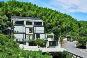 A multi-story building with a flat roof, surrounded by lush greenery and a winding road. - Heshi Mogan Hotel (Deqing)