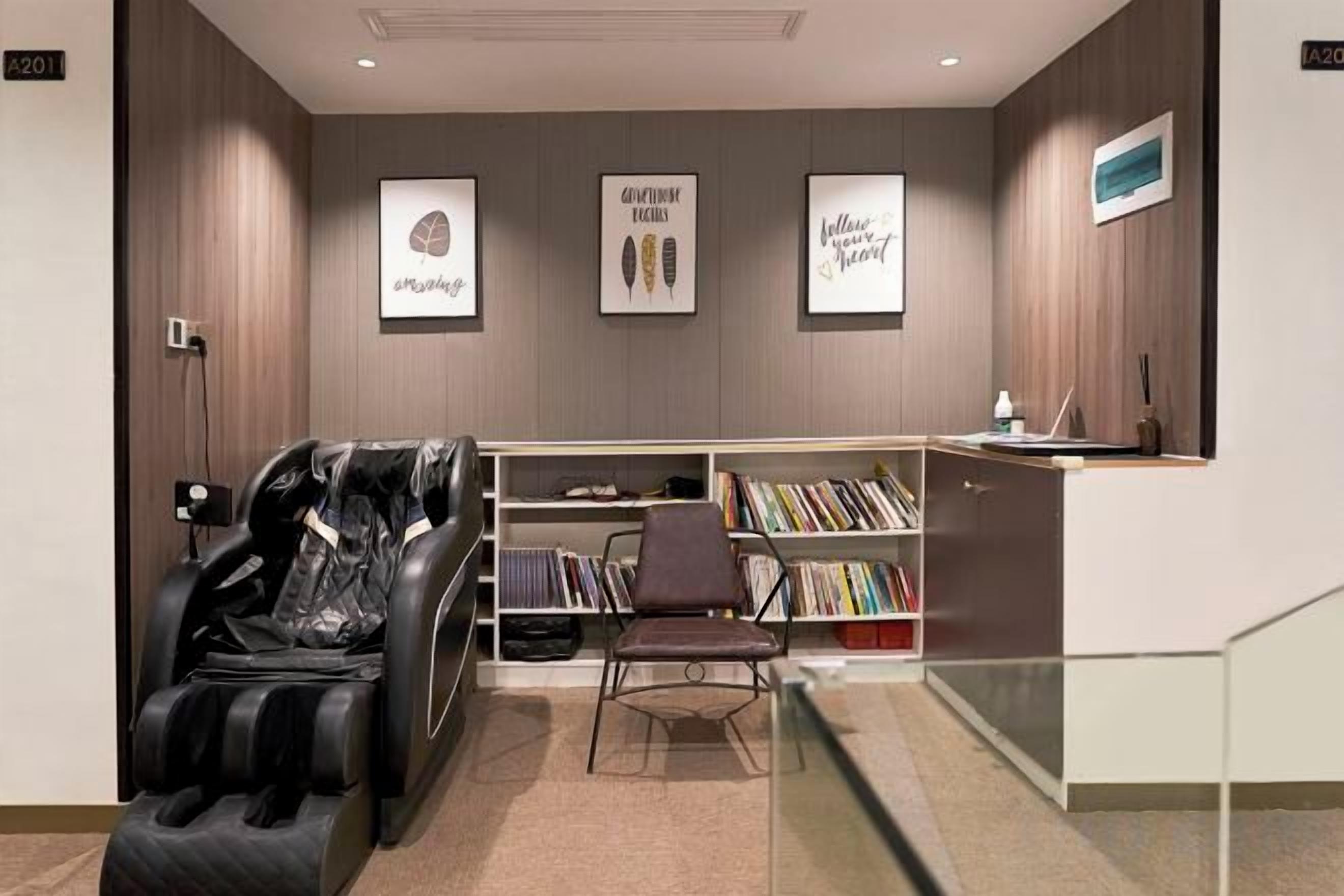 A massage chair, a bookshelf, and a desk with a computer in a modern room.