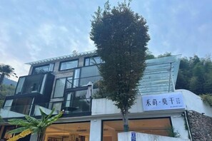 A modern building with a sign in a foreign language, a balcony, and a tree in front. - Heshi Mogan Hotel (Deqing)