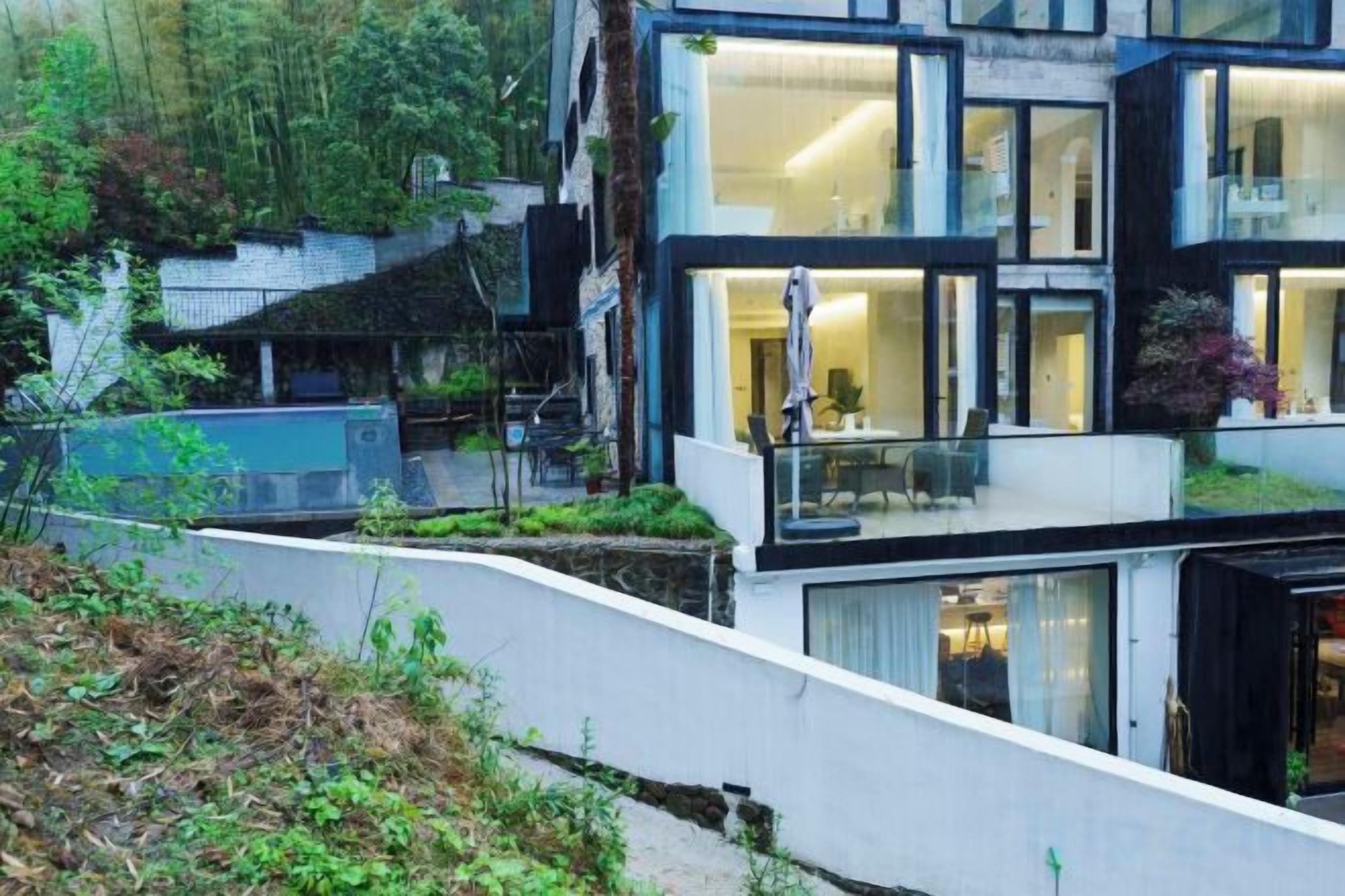 A modern multi-story building with large windows, a balcony, and a garden area.