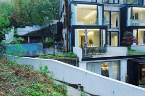 A modern multi-story building with large windows, a balcony, and a garden area. - Heshi Mogan Hotel (Deqing)