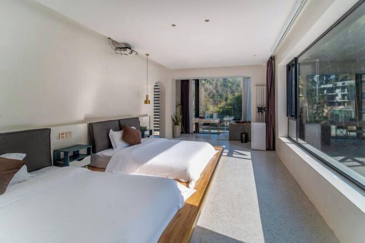 A modern hotel room with two beds, a large window, and a balcony.