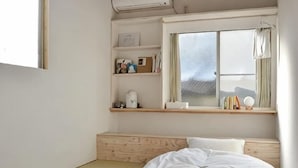 Une chambre à coucher au style minimaliste, avec un lit, une fenêtre donnant sur un beau paysage et une étagère où sont exposés des objets personnels.