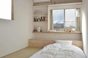 Un dormitorio minimalista con una cama, una ventana con vistas y un estante con objetos personales.