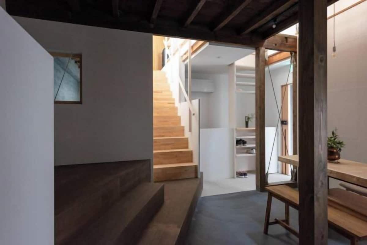 Un intérieur moderne avec un escalier menant à un deuxième étage, un banc en bois et une petite table agrémentée d’une plante.
