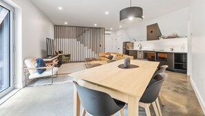 Una cocina moderna con una mesa y sillas de madera, una lámpara colgante y una escalera que sube a otro nivel.