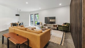 Una sala de estar moderna con sofá, banca, televisor y una zona de comedor con sillas y una mesa.