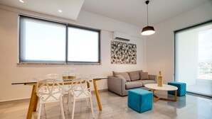 Una sala de estar moderna con una mesa de comedor de vidrio, sillas blancas, un sofá gris y otomanas azules.