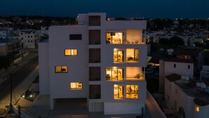 Un edificio moderno de varios pisos con ventanas y balcones iluminados, rodeado de una zona residencial.