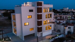 Un moderno edificio de varios pisos con balcones y ventanas amplias, rodeado de otras edificaciones residenciales.