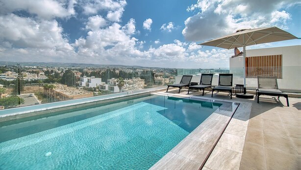 Una piscina infinita en la azotea con agua cristalina y azul, rodeada de sillones de descanso y una sombrilla.