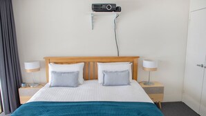 A hotel room with a bed, two bedside tables with lamps, a wall-mounted air conditioning unit, and a door. - Torndirrup Seascape - Albany (Albany)