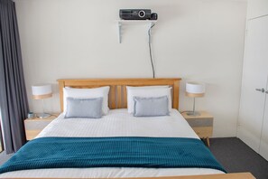 Ein Hotelzimmer mit einem Bett, zwei Nachttischen mit Lampen, einer Wand-Klimaanlage und einer Tür.