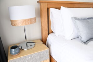 A neatly made bed with white bedding, a grey pillow, and a wooden headboard.
