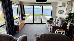 A living room with a sofa, a coffee table, and a view of the sea through large windows. - Torndirrup Seascape - Albany (Albany)
