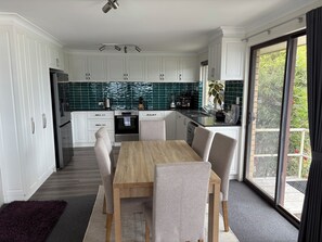 Eine moderne Küche mit weißen Schränken, einem Holztisch und Blick auf Grünflächen.