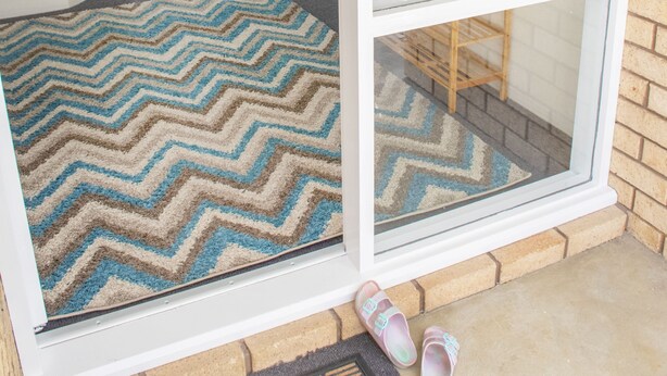 A hallway with a chevron-patterned rug leading to a door, a window with a view of a brick wall, and a pair of slippers on the floor. - Torndirrup Seascape - Albany (Albany)