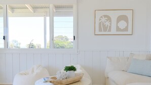 Ein Zimmer mit einem weißen Sofa, einem runden Tisch mit Schüssel und Pflanze sowie einem gerahmten Bild an der Wand.