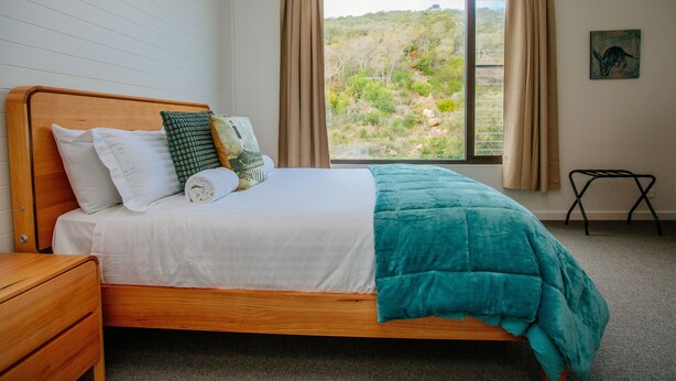 A bedroom with a wooden bed, beige curtains, and a view of a hilly landscape. - Welcome to Whale Song (Middleton Beach)