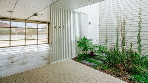 A modern interior with a large window, a white partition, and a small garden area with plants. - Welcome to Whale Song (Middleton Beach)