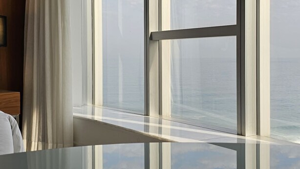 A modern room with a large window, a glass table, and a view of the sky and clouds. - Mais que um Hotel, uma Obra de Arte (São Conrado Rio de Janeiro)