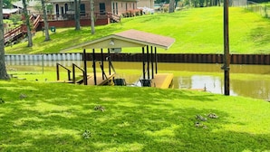 A house with a dock extending over a pond, surrounded by lush green grass and trees.