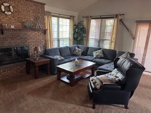 Una sala de estar con chimenea de ladrillo, un sofá modular, un sillón de cuero y una mesa de centro.