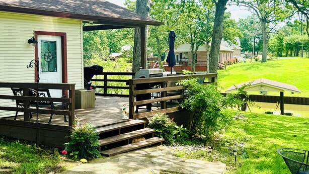 A wooden deck with outdoor furniture, a covered patio area, and a view of a green landscape with trees.