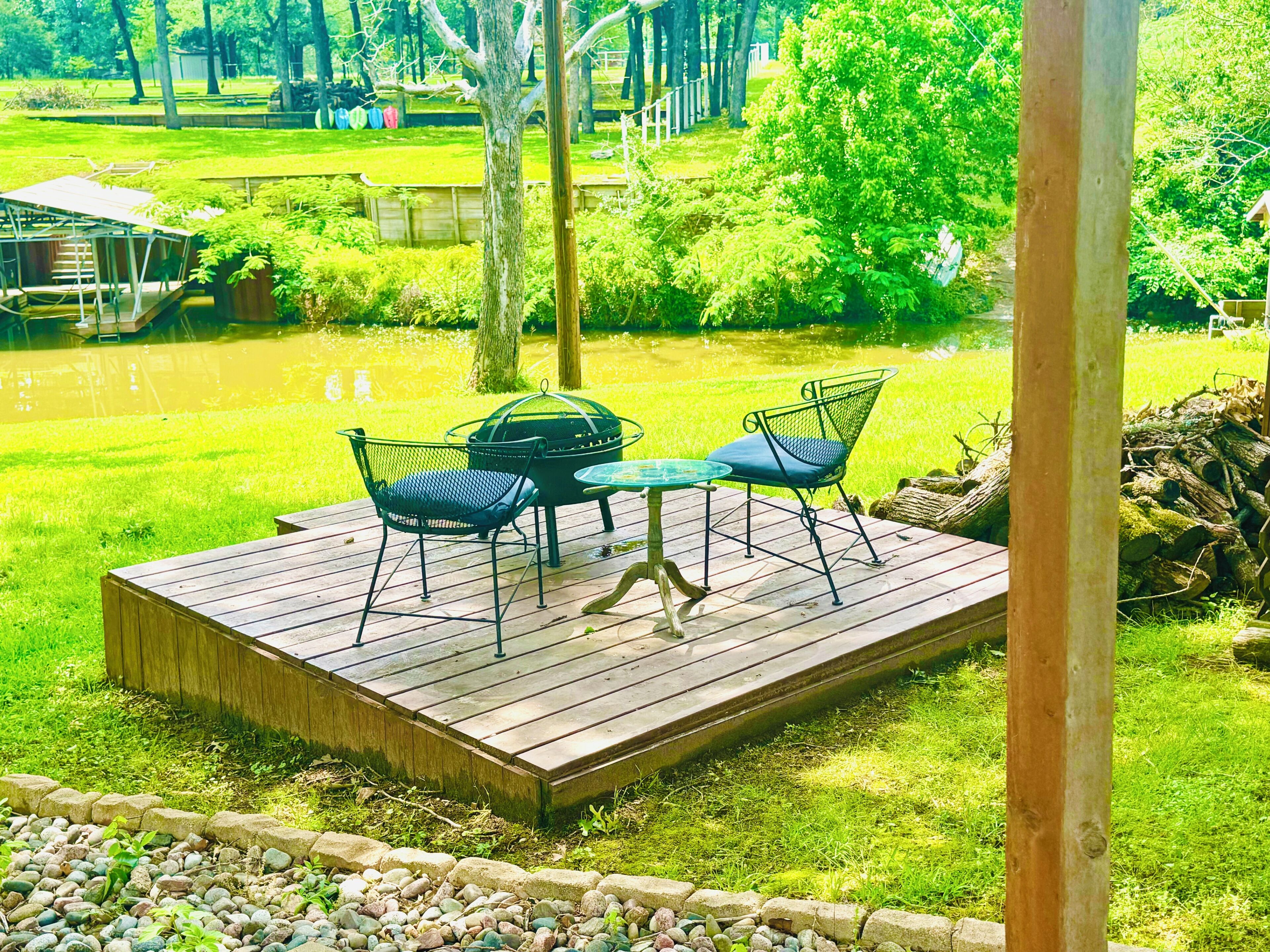 A wooden deck with a table and chairs, surrounded by a grassy area and trees.