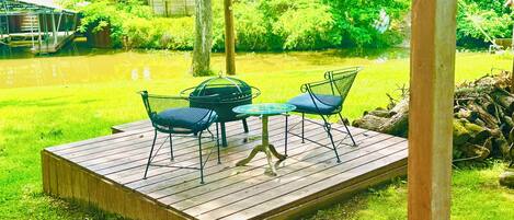 A wooden deck with a table and chairs, surrounded by a grassy area and trees.