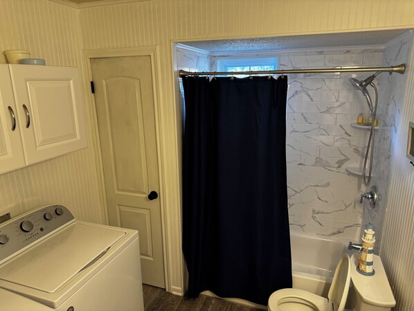 Un baño con puerta blanca, lavadora, bañera con ducha e inodoro.