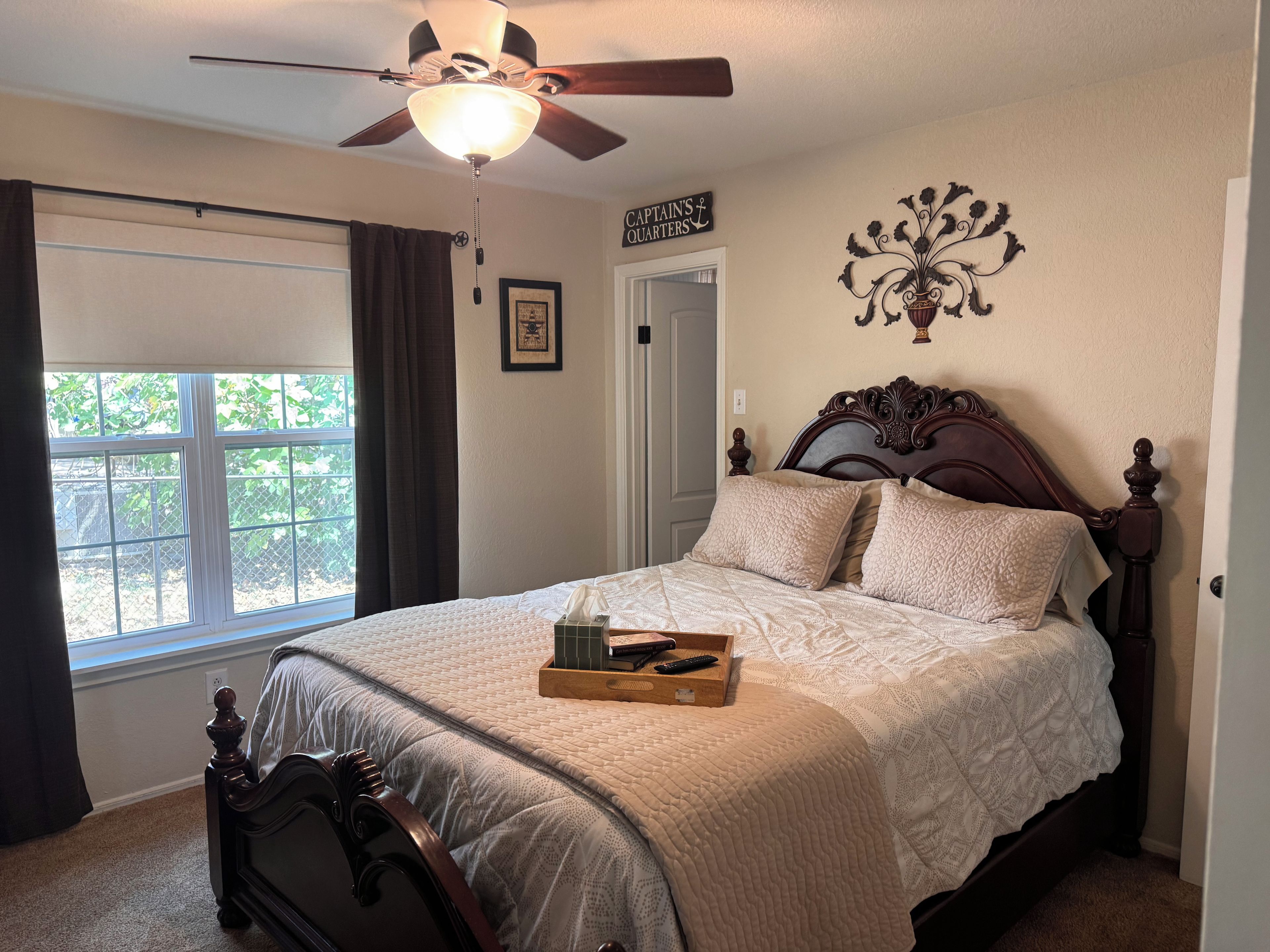 A bedroom with a bed, a ceiling fan, a window, and a door.