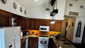 A kitchen with wooden cabinets, a white refrigerator, a microwave, and a coffee maker. There is a sign that says "NO HURRIES NO WORRIES" and a "WELCOME" sign on the wall.