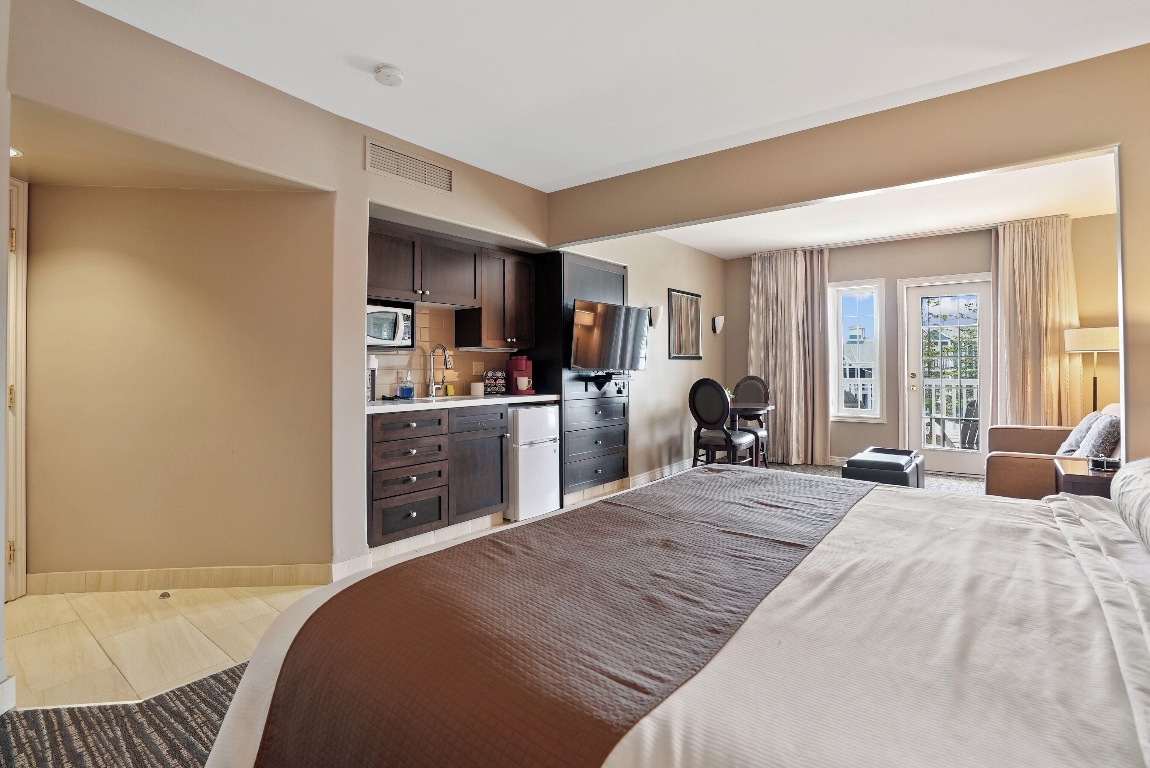 A hotel room with a large bed, a kitchenette, a TV, and a view of the outdoors.