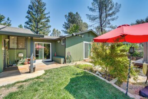 A green house with a patio, a red umbrella, and a small tree. - Hot Tub, Dog-Friendly Yard! 3-Acre Redding Retreat (Redding)