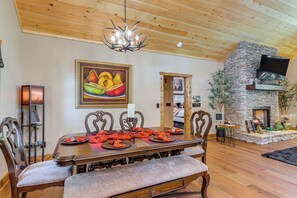 A dining area with a wooden table, chairs, and a chandelier. There is a stone fireplace and a television mounted on the wall. - 'Next Stop Heaven' Game Room & Multiple Decks (Ellijay)