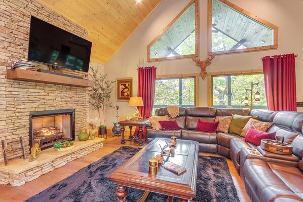 A cozy living room with a stone fireplace, leather sofa, and a large TV mounted on the wall. - 'Next Stop Heaven' Game Room & Multiple Decks (Ellijay)
