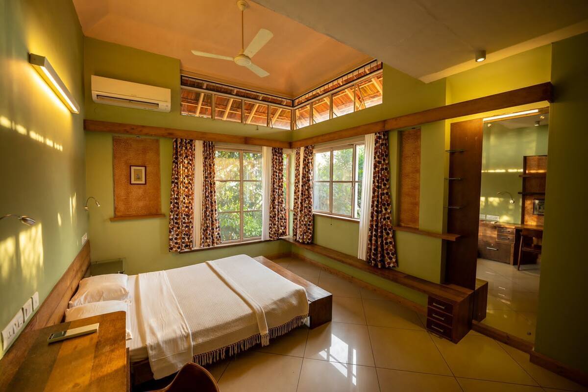 A bedroom with a bed, a desk, a chair, a ceiling fan, and a window with curtains.