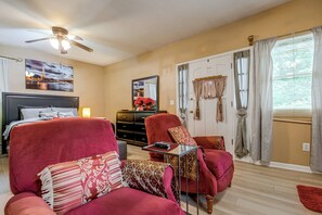 A hotel room with a bed, two armchairs, a dresser, a ceiling fan, a window with curtains, and a painting of the Eiffel Tower. - Charming Stone Mountain Studio: Deck & No Steps (Stone Mountain)