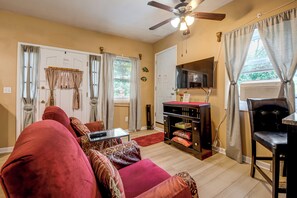 A living room with a red sofa, a small table, a ceiling fan, and a TV on the wall. - Charming Stone Mountain Studio: Deck & No Steps (Stone Mountain)