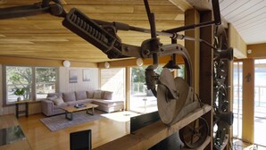 Ein Zimmer mit Holzboden, einem großen Fenster, einer Couch, einem Tisch und einer technischen Vorrichtung.