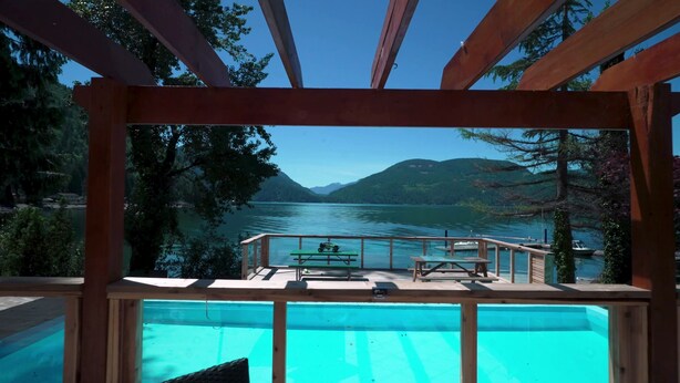Eine Holzterrasse mit Pool, Blick auf einen See mit Bergen im Hintergrund.